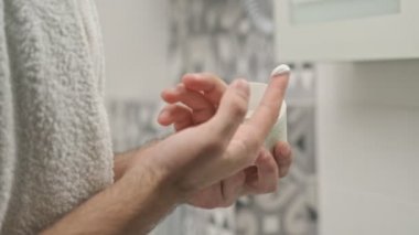 Omzunda havluyla banyodaki aynaya bakarken yüzüne krem süren sakin, yakışıklı, üstsüz bir adamın yan görüntüsü.