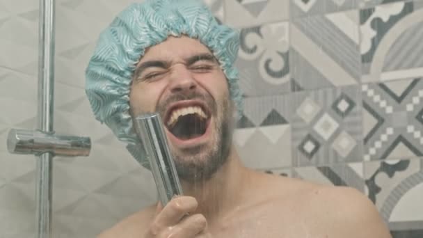 シャワーを浴びながら彼の手の中にシャワーヘッドで歌う面白いですハンサムな若いです裸の男のビューを閉じる — ストック動画