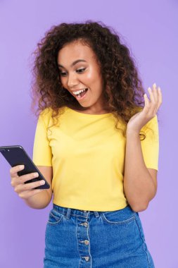 Kıvırcık saçlı, gülümseyen ve elinde akıllı telefon tutan Afro-Amerikan kadını.