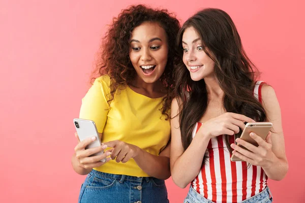 Imagen de chicas multinacionales emocionadas sonriendo y mirando juntos los teléfonos celulares — Foto de Stock