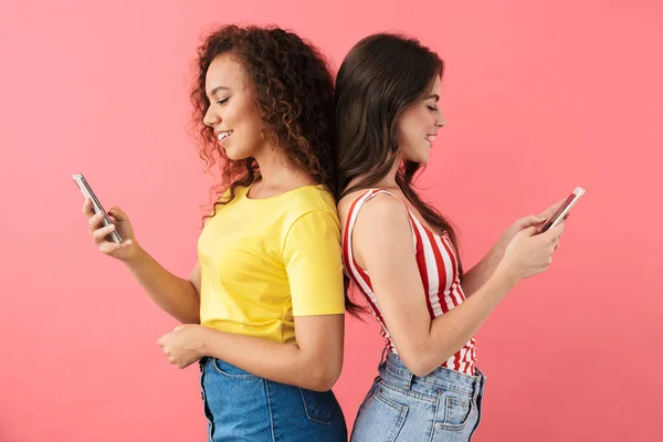 Image of pretty multinational girls looking at cellphones standing back to back — Stock Photo, Image