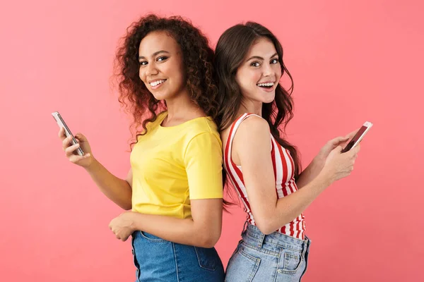 Imagen de chicas morenas multinacionales sosteniendo teléfonos celulares espalda con espalda — Foto de Stock