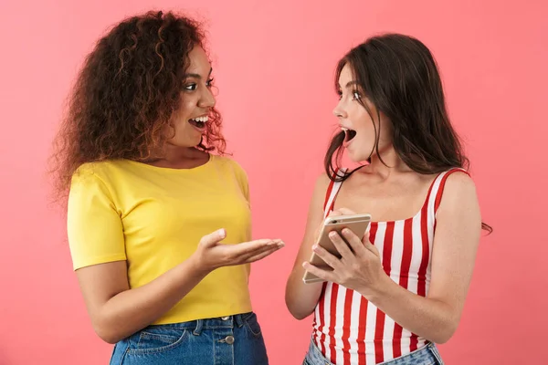 Imagen de chicas multinacionales sorprendidas sonriendo y sosteniendo los teléfonos celulares juntos —  Fotos de Stock