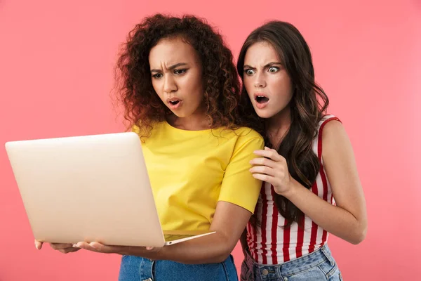Imagen de chicas multinacionales sorprendidas preguntándose y sosteniendo computadora portátil — Foto de Stock