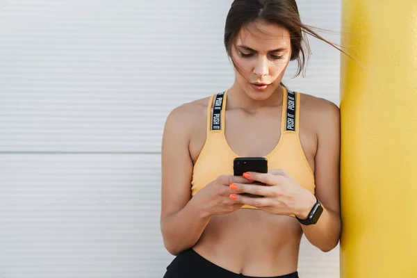 Imagen de mujer atlética en ropa deportiva sosteniendo el teléfono celular al aire libre — Foto de Stock