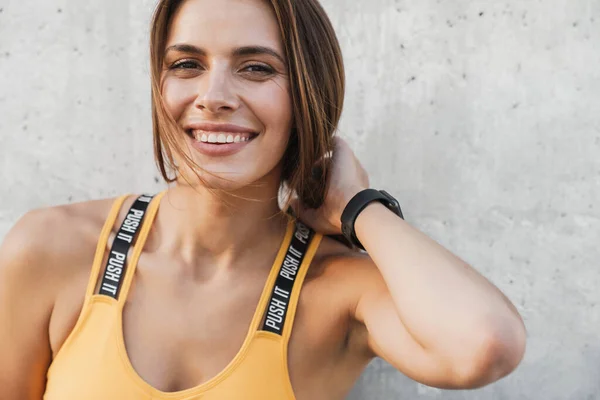 Immagine di donna felice in abbigliamento sportivo sorridente sopra il muro di cemento ou — Foto Stock