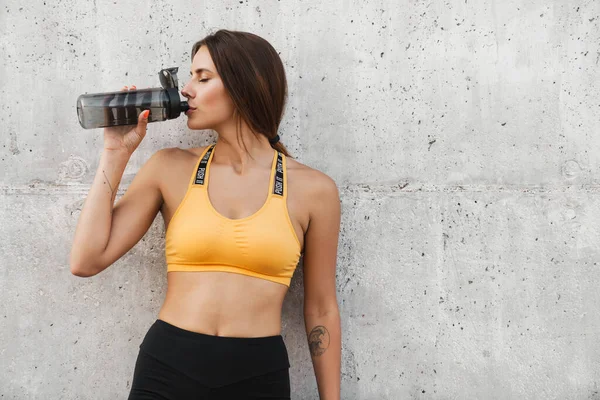 Image de femme fitness en tenue de sport boire de l'eau sur du béton — Photo