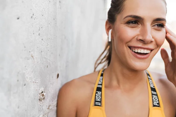 Imagem de mulher morena sorrindo e tocando fones de ouvido ao ar livre — Fotografia de Stock