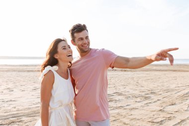 Yazlık giysiler giyen genç ve güzel bir çift sahilde dikiliyor.