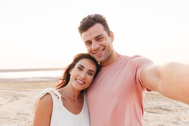 Yazlık giysiler giyen genç ve güzel bir çift sahilde dikiliyor.