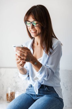 İyimser, güzel bir iş kadını. Evde, mutfakta cep telefonuyla sohbet ediyor..