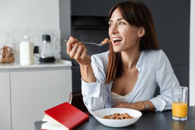 Olumlu iyimser kadın evde, mutfakta kahvaltı yapıyor mısır gevreği yiyor..