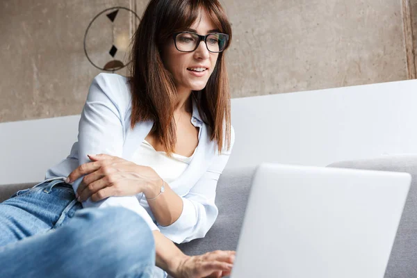 Positive business woman indoors at home on sofa using laptop computer. — Stock Photo, Image