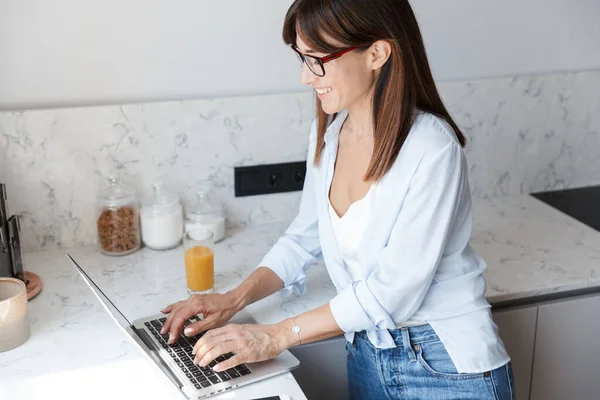 Усміхнена ділова жінка вдома на кухні використовує ноутбук . — стокове фото