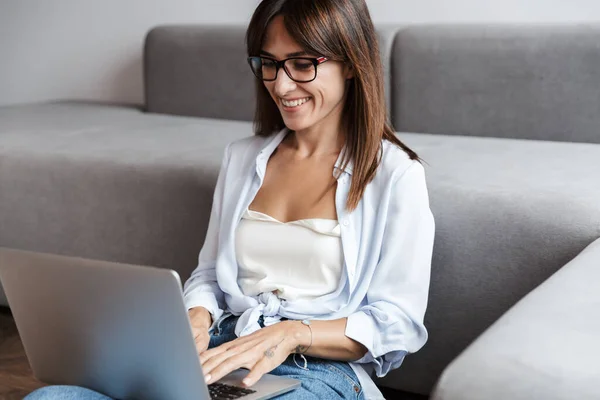 Gelukkig zakenvrouw binnen thuis op vloer in de buurt van bank in de woonkamer met behulp van laptop computer. — Stockfoto