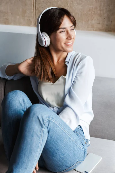 家里积极快乐的女人坐在客厅的沙发上，用耳机听音乐. — 图库照片