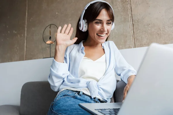 Lächelnde junge Frau winkt Freunden zu, die sich per Laptop unterhalten. — Stockfoto