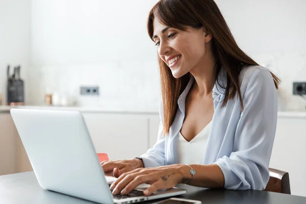 Feliz mulher alegre dentro de casa na cozinha usando computador portátil . — Fotografia de Stock