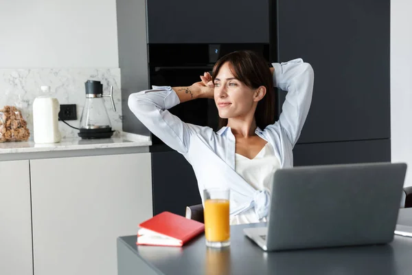 La mujer positiva en el interior en casa en la cocina usando el ordenador portátil descansan relajadamente . — Foto de Stock
