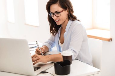 Ofisteki fotoğrafçı kadın, dizüstü bilgisayar ve grafik tabletle çalışan kamera lensleriyle masada oturuyor..
