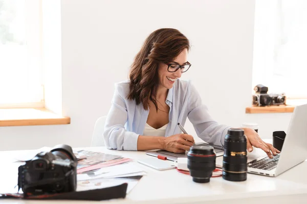Photographe femme au bureau assis à la table avec des lentilles de caméra travaillant par ordinateur portable et tablette graphique . — Photo