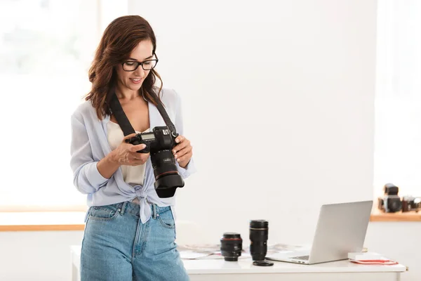 Optymistyczna młoda fotograf kobieta w biurze trzyma aparat. — Zdjęcie stockowe