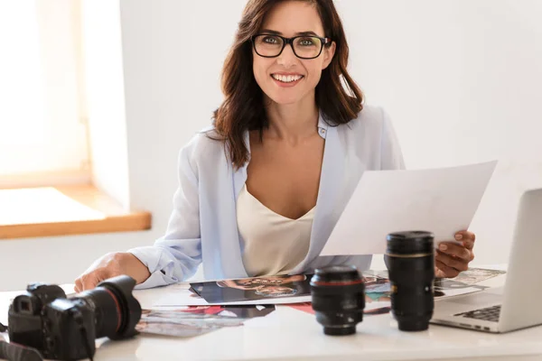 オフィスのきれいな写真家の女性は、カメラと仕事中の写真とテーブルに座っている. — ストック写真
