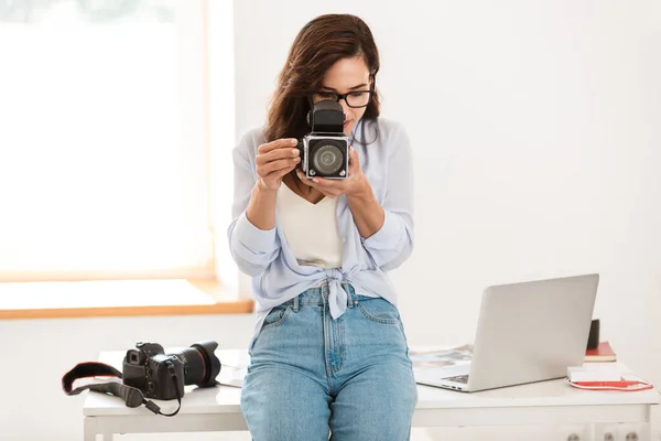 Increíble joven bonita fotógrafa mujer en la oficina sosteniendo la cámara vieja retro . — Foto de Stock