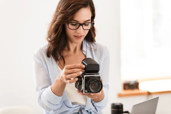 Ofisteki genç, güzel fotoğrafçı kadın elinde eski bir fotoğraf makinesi tutuyor.. — Stok fotoğraf