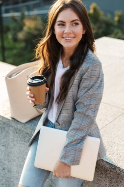 Mutlu genç iş kadını elinde dizüstü bilgisayarla kahve içiyor..