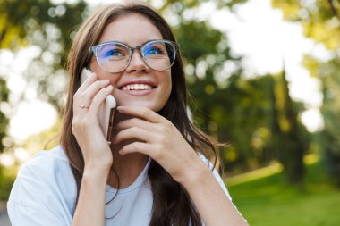 Doğal yeşil parktaki bayan cep telefonuyla konuşuyor..