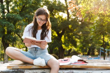 Doğa yeşili parkta bir kadın deftere notlar yazıyor..