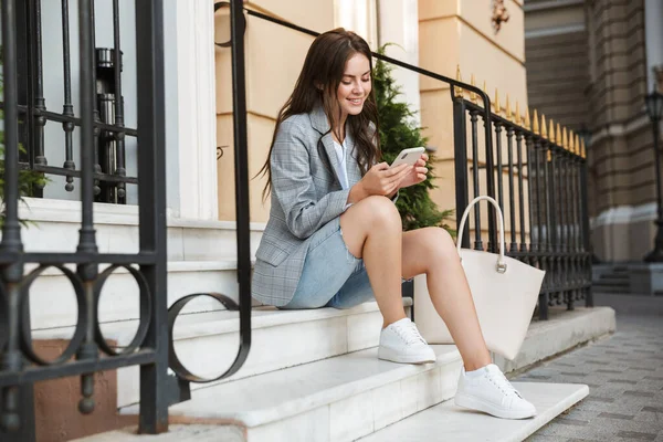 Obchodní dáma venku na ulici pomocí mobilního telefonu sedět na schodech. — Stock fotografie