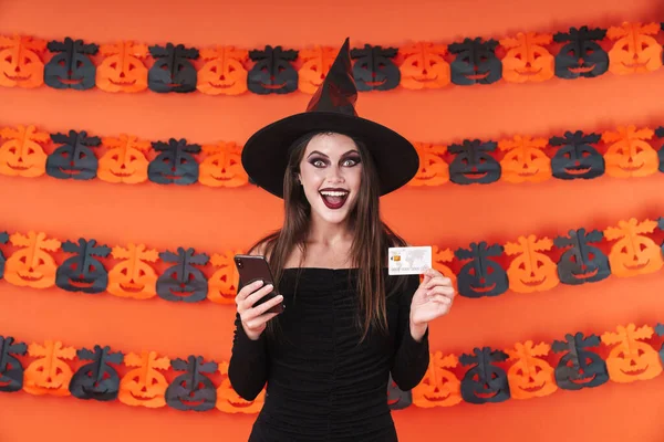 Imagem da bruxa menina em traje halloween segurando telefone e credi — Fotografia de Stock