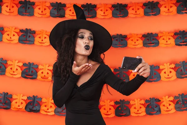 Imagen de linda chica bruja en traje de halloween negro tomando selfi —  Fotos de Stock