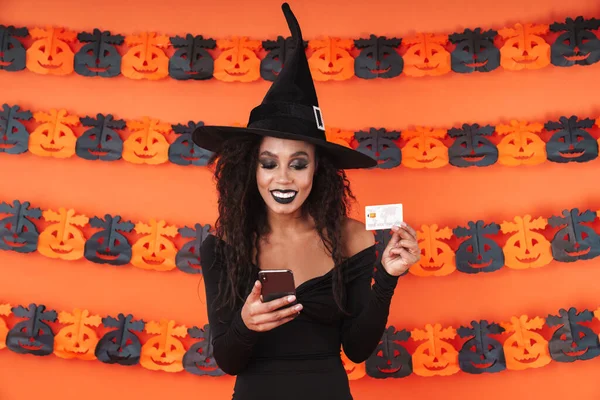 Imagem da bruxa menina em traje halloween segurando telefone e credi — Fotografia de Stock