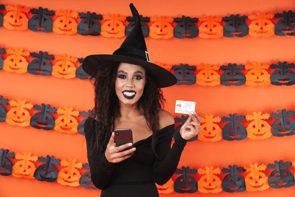 Imagem da bruxa menina em traje halloween segurando telefone e credi — Fotografia de Stock