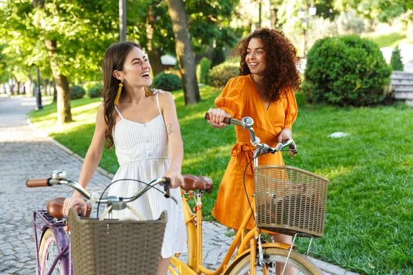 Zwei ziemlich glückliche Mädchen in Sommerkleidern auf Fahrrädern — Stockfoto