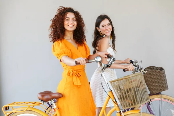 Two pretty happy girls wearing summer dresses riding bicycles — Stock Photo, Image