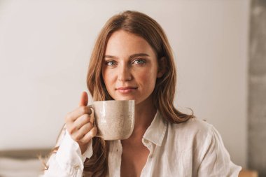 Zencefilli iş kadını ofiste oturup kahve içiyor..