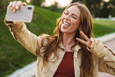 Gülümseyen genç kızıl kadın cep telefonuyla selfie çek..