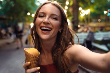 Güzel, genç, kızıl bir kadın kamerayla selfie çeker dondurma yer..