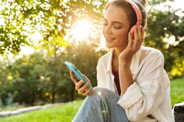 Güzel bir genç kız, sıradan giyinmiş, bankta oturuyor.