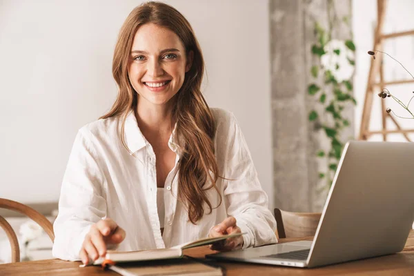 Pretty business woman using laptop computer holding notebook. — Stock Photo, Image