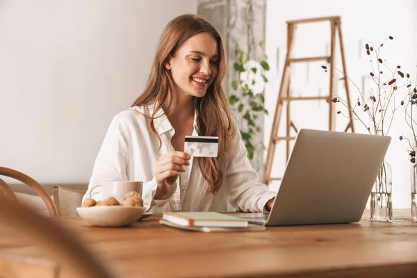 신용 카드를 들고 있는 노트북 컴퓨터를 사용하여 사무실에 앉아 있는 여성. — 스톡 사진