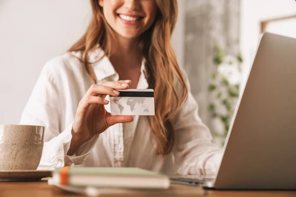 신용 카드를 들고 있는 노트북 컴퓨터를 사용하여 사무실에 앉아 있는 여성. — 스톡 사진