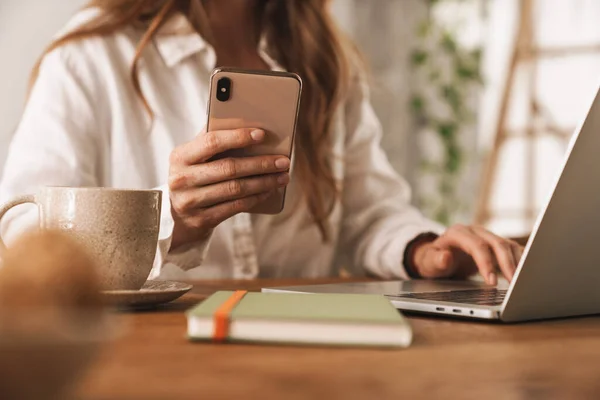 Zakelijke vrouw zitten binnen in kantoor met behulp van laptop computer en mobiele telefoon. — Stockfoto