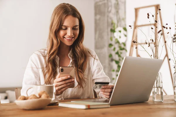 Woman using laptop computer and mobile phone holding credit card. — Stock Photo, Image