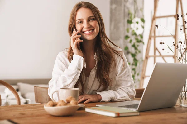 Mulher de negócios sentar-se dentro de casa no escritório usando computador portátil tomando por telefone móvel . — Fotografia de Stock