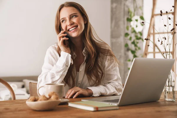 Business woman sit indoors in office using laptop computer taking by mobile phone. — Stock Photo, Image